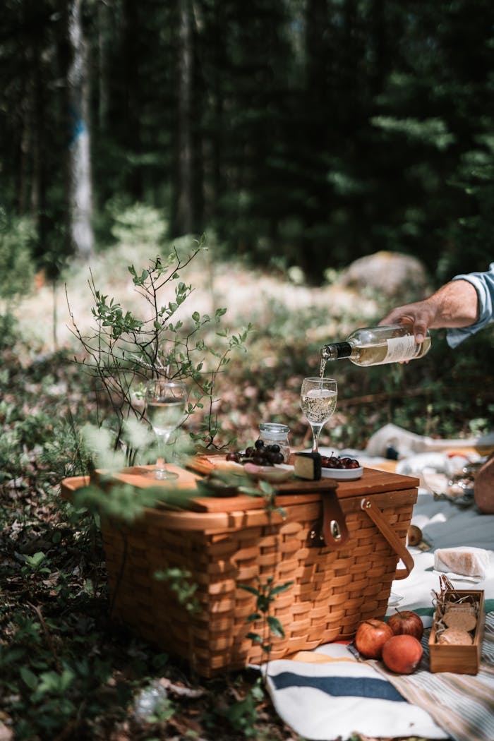 about-02 A serene picnic setup in the woods with wine being poured, surrounded by nature.